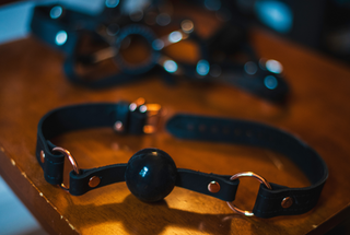 Black leather gag with a round metal buckle on a wooden surface